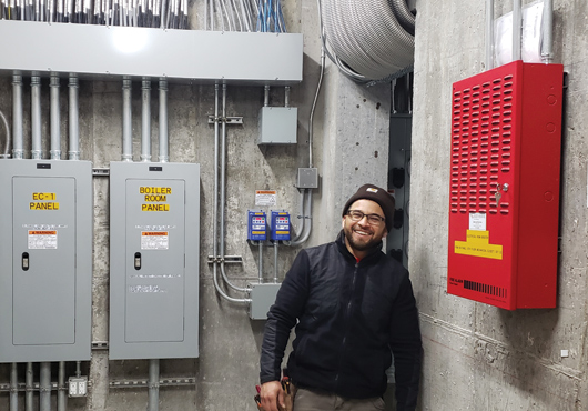 Foreman Mario Umanzor proudly displays the main breakers and fire alarm system in a large apartment building.