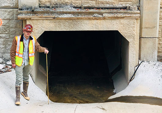 Project Manager Konner Horton stands next to an 8-foot by 6-foot culvert that was grouted to fill voids, stabilize the soil to stop water inflows and prevent settlement.