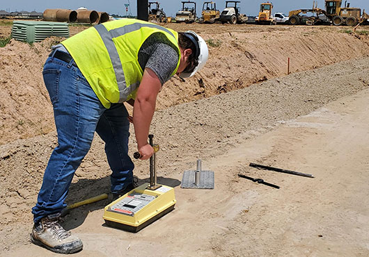 A PACS Construction Laboratories and Testing Services, Inc. technician tests subgrade for compaction and moisture content to determine whether it is compliant.