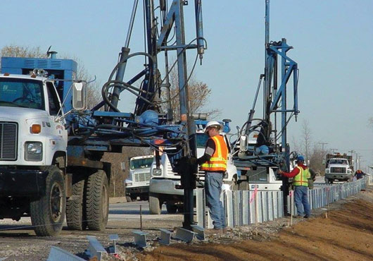 A crew from Nationwide Construction Group uses truck-mounted pile drivers to install guardrail posts along a highway for the Michigan Department of Transportation. 