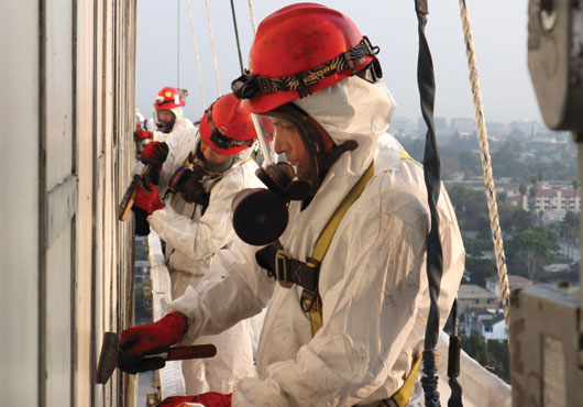 Quality Environmental, Inc. team members use a swing stage basket while removing polychlorinated biphenyls (PCBs) from the exterior of a building.