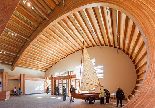 Between the wood ceiling panels at the Mystic Seaport Museum in Connecticut, acoustical panels made of a cementitious wood fiber are attached to the roof deck with an air pocket between them. The panels are painted to blend with the wood.