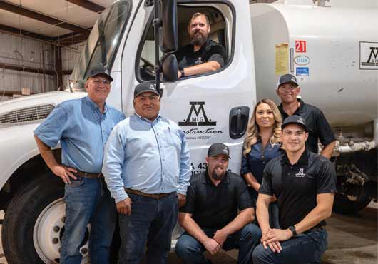 The M-Mig Construction, Inc. leadership team (from left to right): Mark Migliazzo, Dairy/Commercial Project Manager; Genaro Campos, Dairy Project Manager; James Jantz (in cab), Operations Manager; Brandon Johnson, Project Supervisor;  Jessica Saavedra, Office Manager; Alberto Perez, Assistant Office Manager and Matt Migliazzo, Owner and President (standing, far right).