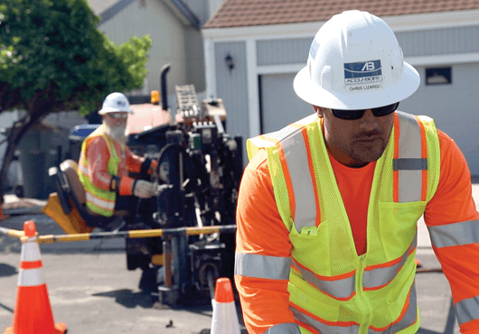 In the background, an Accu-Bore worker operates a Ditch Witch directional drill to install new gas service for a residence.